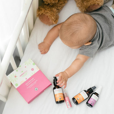 A baby playing with our products contained within our Bun in the Oven Kit, including our Oh Baby! Belly Oil